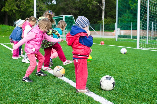 Seis crianças de idades próximas chutando bolas de futebol em um gol