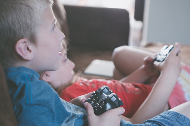 Duas crianças atentas à televisão, com controle em mãos jogando videogame