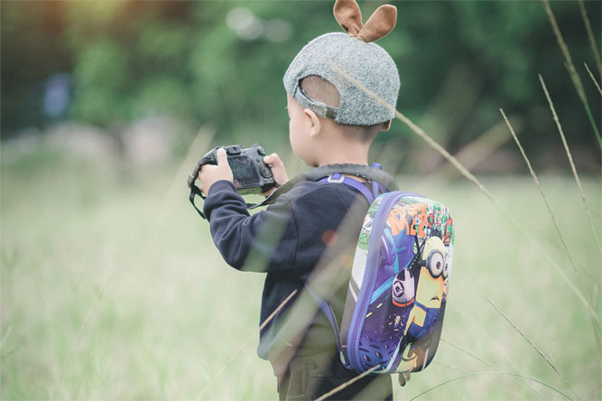 menino de mochila e boné segurando uma máquina fotográfica