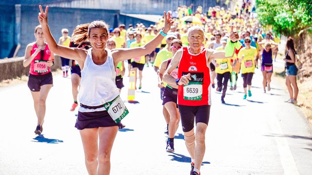 Pessoas correndo uma maratona. Uma delas está com ambos os braços levantados, fazendo um sinal de V com as duas mãos