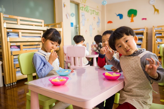 três crianças sentadas ao redor de uma mesa rosa comendo